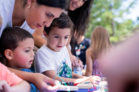 Tow young boys and mother playing with circuit blocks outside 