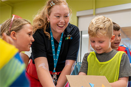 Amazeum team member smiling and interacting with two young kids at summer camp